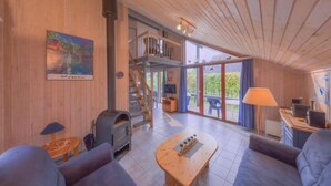 A spacious room with a wooden ceiling, a fireplace, a sofa, a coffee table, and a staircase leading to an upper level. - Ferienhaus im Ferienpark Mirow (Mirow)