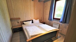 A wooden-paneled bedroom with a bed, bedside tables, and a window with curtains. - Ferienhaus im Ferienpark Mirow (Mirow)