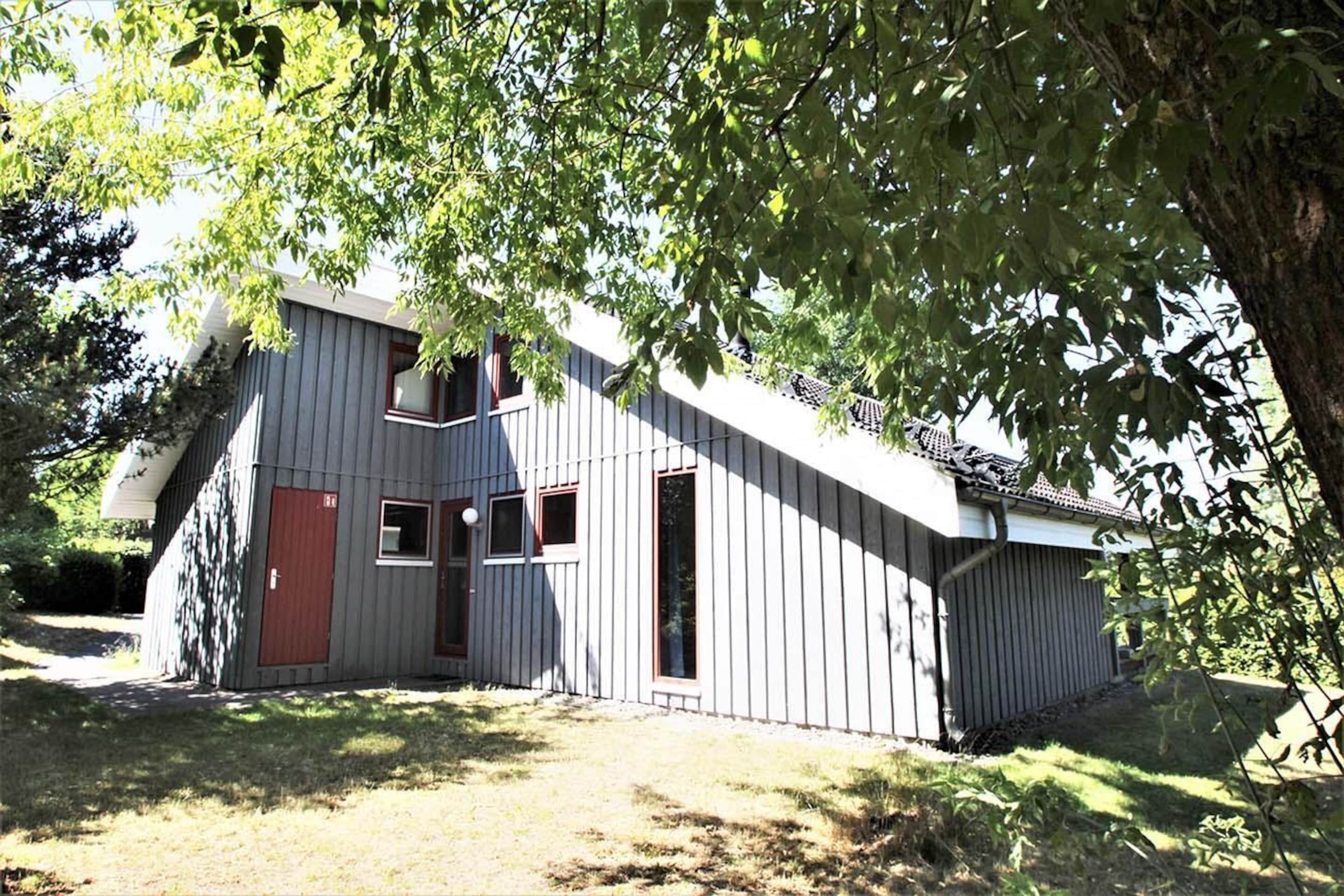 A two-story building with a sloped roof, a red door, and multiple windows.