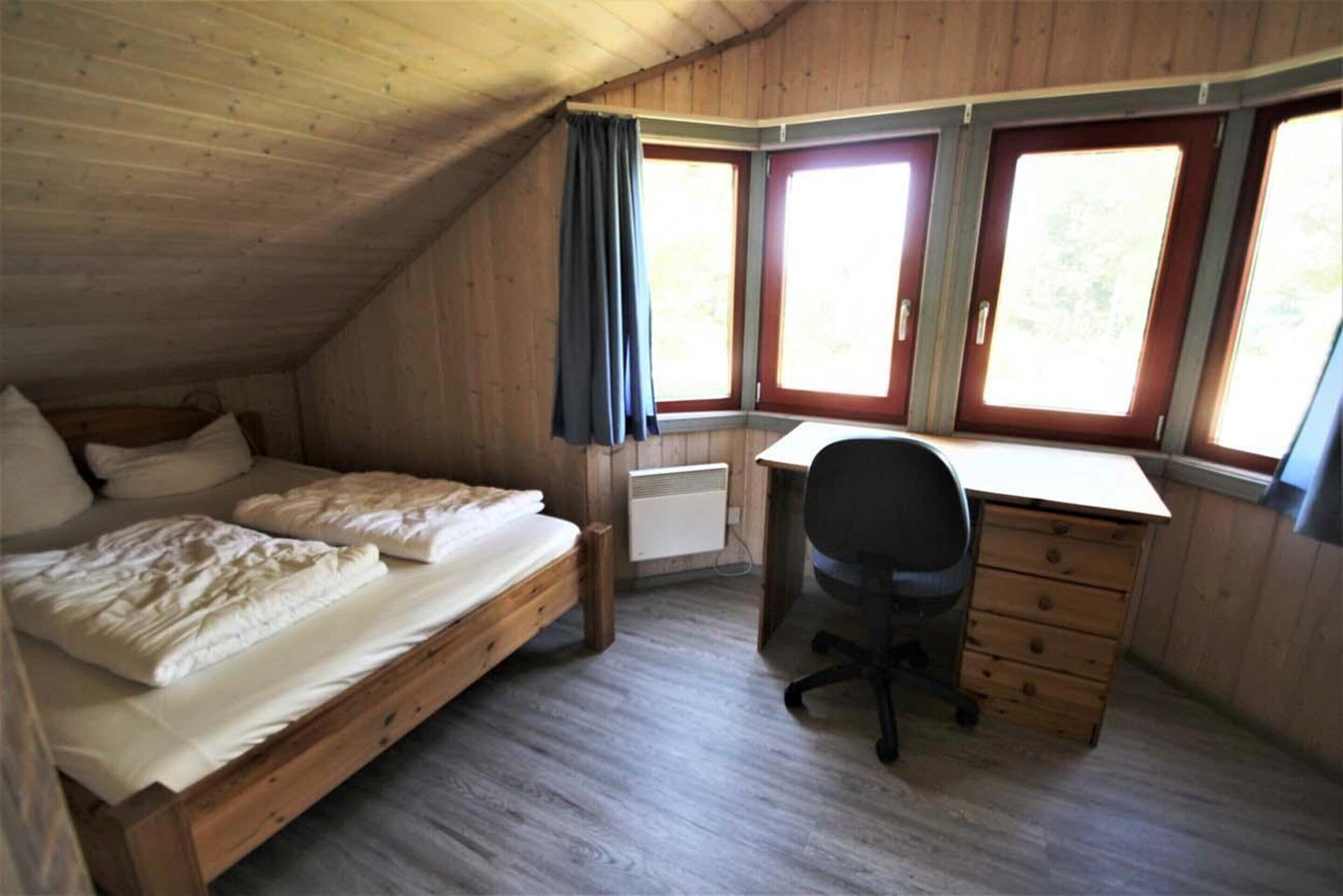 A room with a loft bed, a desk, and a chair. There are three windows with curtains.