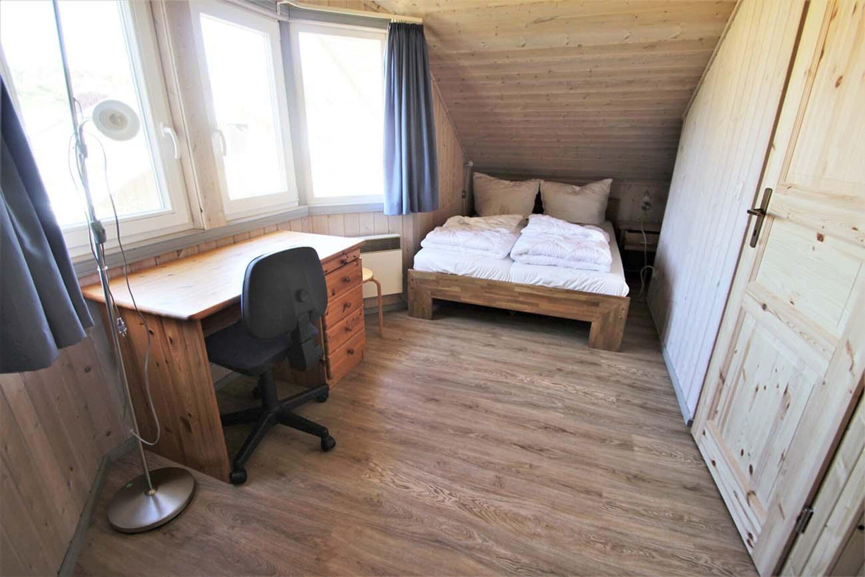 Una habitación pequeña y acogedora con un escritorio de madera, una cama y una ventana.