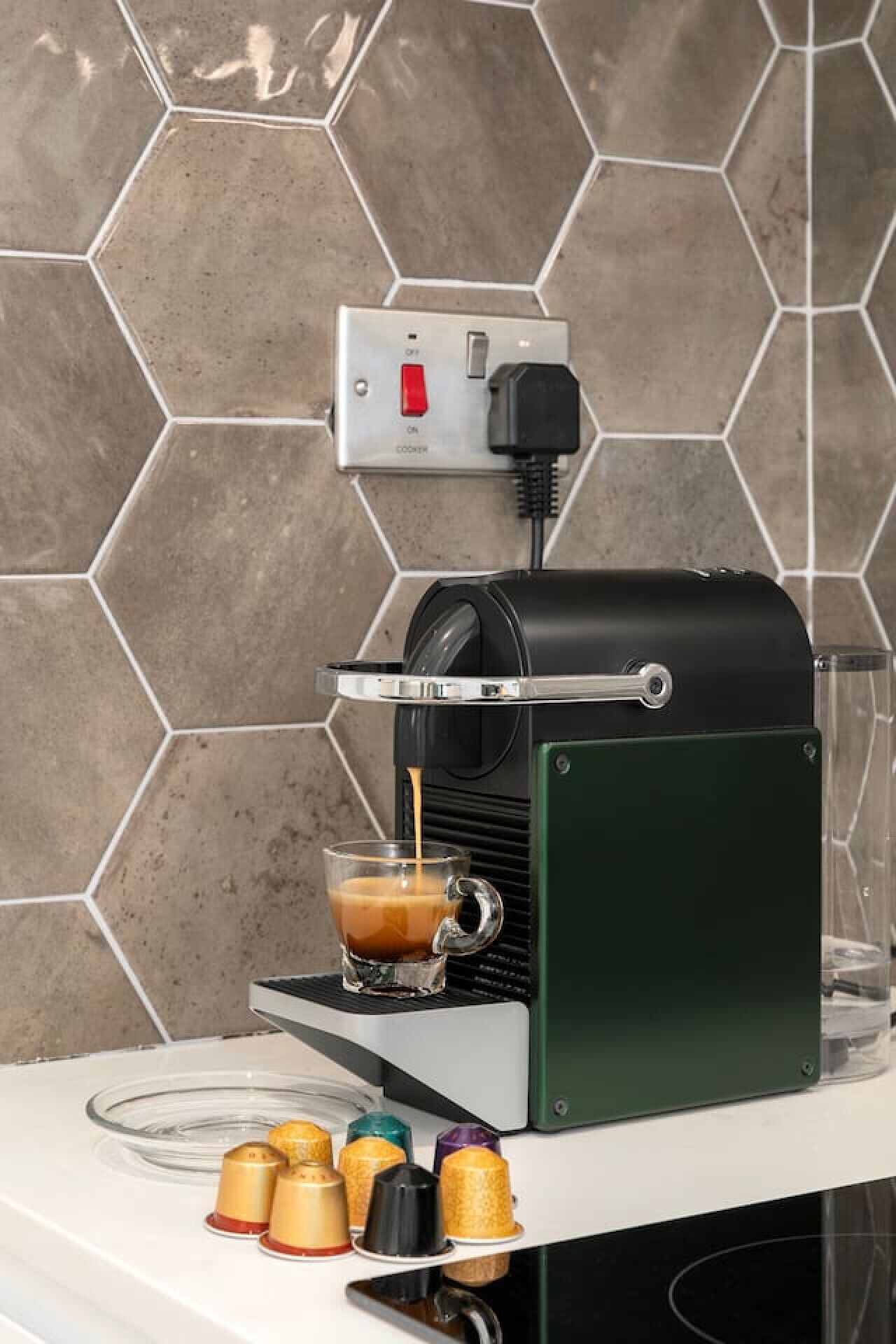 A coffee machine on a countertop with a hexagonal tiled backsplash.