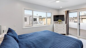 Ein Schlafzimmer mit einem großen Bett, einer Kommode, einem Flachbildfernseher und einer Schiebeglastür zum Balkon.