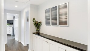Ein Flur mit weißen Schränken, einer schwarzen Arbeitsplatte und einem Blumentopf. An der Wand hängen drei gerahmte Kunstwerke.