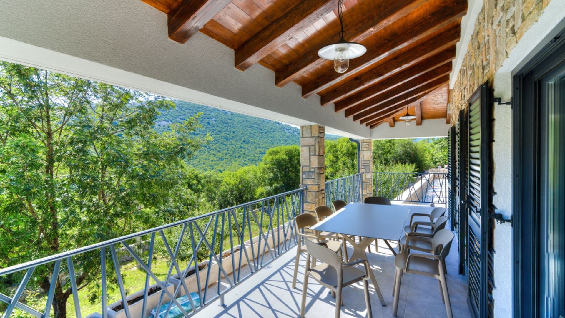A balcony with a table and chairs, overlooking a mountainous landscape.