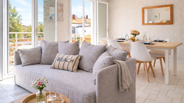 A modern living room with a grey sofa, a dining table with chairs, and a large window offering a view of the outside. - Beautiful 6-person apartment - Arago District (Les Sables-d´Olonne)