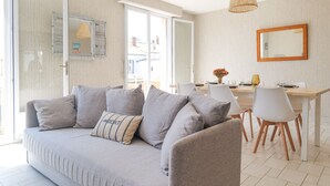 A modern living room with a grey sofa, white dining table, and chairs. - Beautiful 6-person apartment - Arago District (Les Sables-d´Olonne)