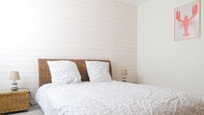 A neatly made bed with a floral-patterned bedspread and two pillows, flanked by wicker nightstands with lamps. - Beautiful 6-person apartment - Arago District (Les Sables-d´Olonne)