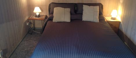 A bedroom with a large bed, two bedside lamps, and a wooden ceiling.