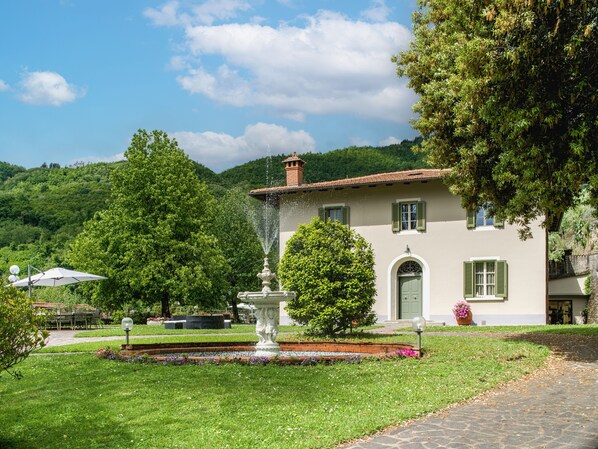 A building with a fountain, surrounded by greenery and a clear sky.