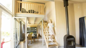 A spacious room with a loft area, a black wood-burning stove, and a dining area with a table and chairs. - Ferienhaus im Skandinavischen Stil (Mirow)