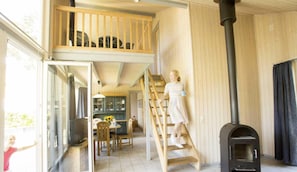 Un intĂ©rieur de chalet chaleureux avec une chambre en mezzanine, un coin repas et un poĂȘle Ă bois.