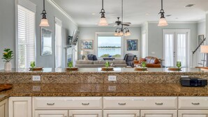 A kitchen with granite countertops, white cabinets, and a central island. There are pendant lights, a ceiling fan, and a view of the outdoors through large windows. - Waterfront! Incredible Views, Watch the Dolphins Play, Perfect for Groups, $300 in Free Tickets! (St. Augustine)