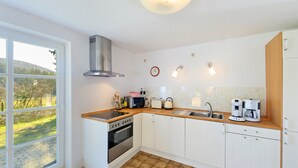 Una cucina moderna con mobili bianchi, una cappa in acciaio inossidabile, forno integrato, microonde, bollitore e macchina da caffè.