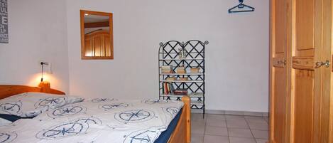 Un dormitorio con cama, armario, espejo y estantería con libros y objetos decorativos.