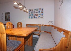 A dining area with a wooden table and chairs, a bench, and a wall decorated with photographs. - Apartment in Wenkendorf for 6 Personen (Fehmarn)