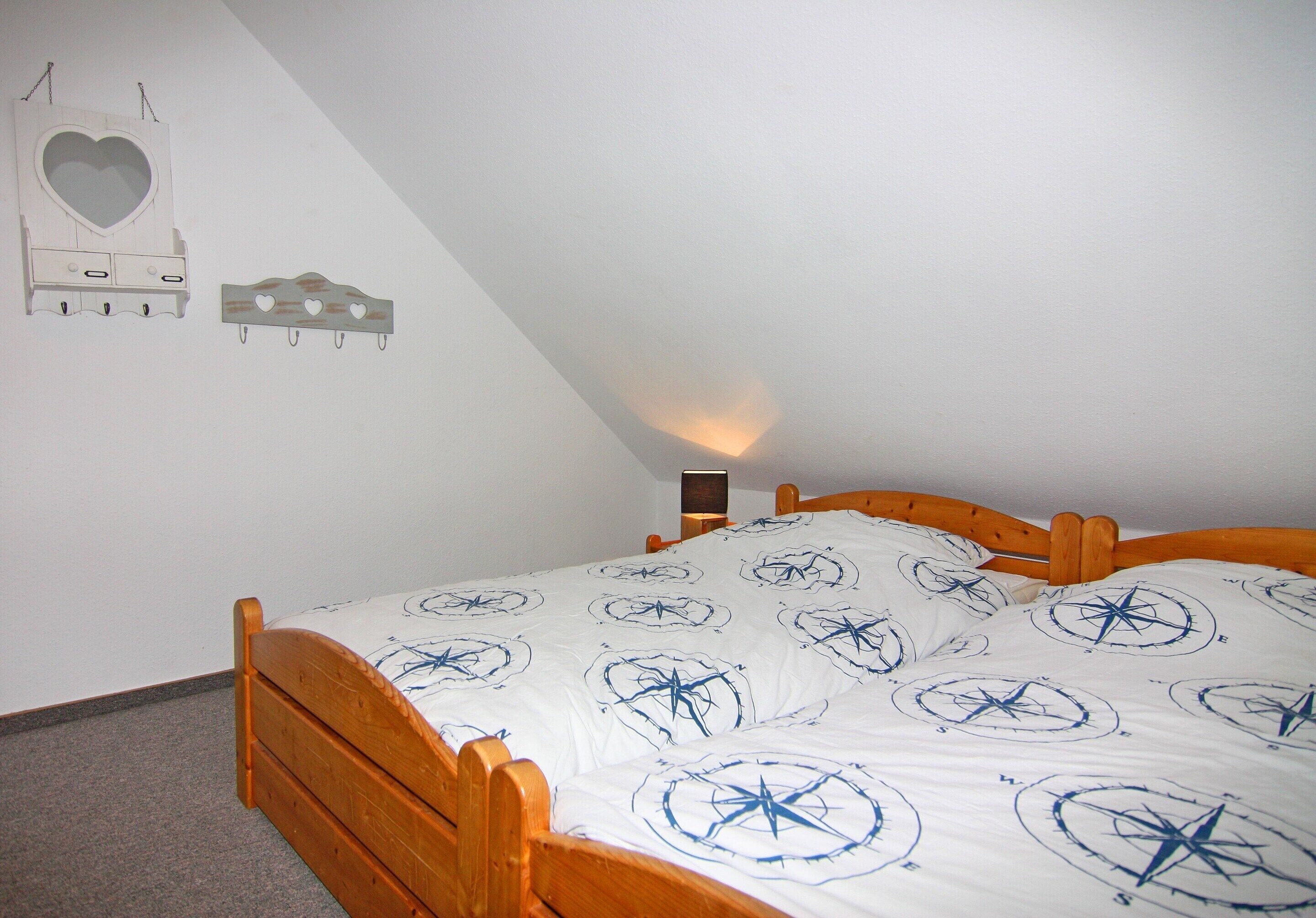 A bedroom with a wooden bed, a white wall with a heart-shaped mirror and a wall-mounted clock, and a bedside table with a lamp.