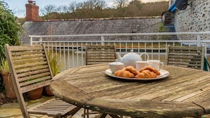 A wooden table with a plate of croissants and tea set on a balcony with a view of a house and trees.