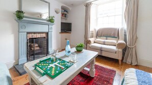 A cozy living room with a fireplace, a sofa, a coffee table with a board game, and a television.