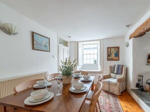 A dining area with a wooden table set for four, white chairs, a potted plant, and a window with a view. - Beautiful private villa for 6 guests with WIFI, TV, patio and pets allowed (Portloe)