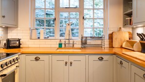 A kitchen with a large window, white cabinets, a wooden countertop, a sink, and a stove.
