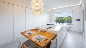 A modern kitchen with a wooden dining table, white cabinetry, and a large window offering a view of greenery. - Wonderful private villa for 10 people with WIFI, hot tub, private pool, A/C and panoramic view (Terranuova Bracciolini)
