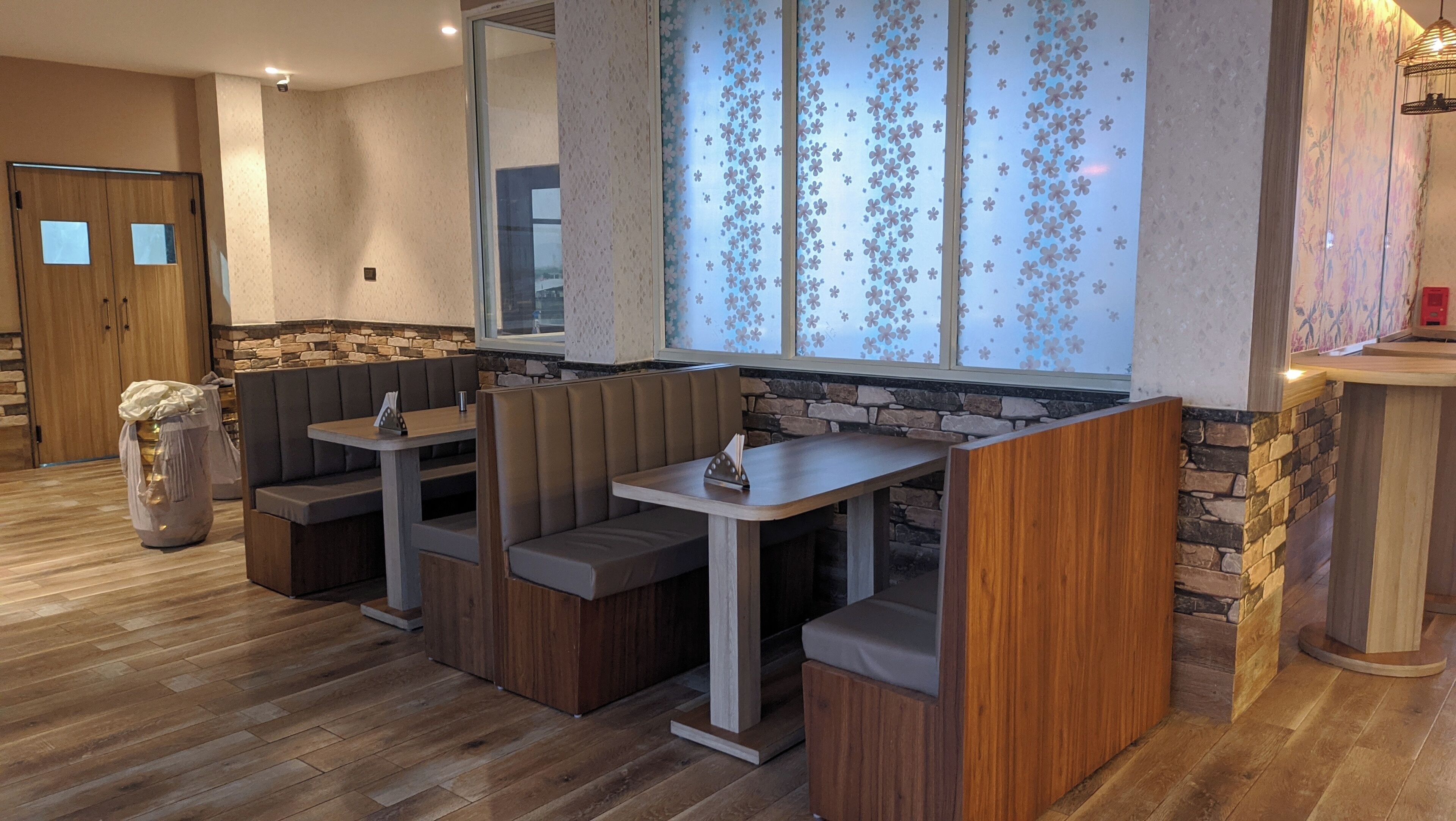 A restaurant with wooden flooring, stone accents, and a large window with floral patterns.