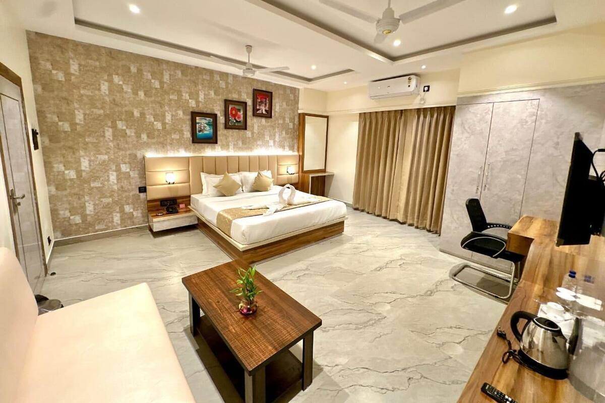 A modern hotel room with a large bed, a wooden coffee table, a desk with a kettle, and a TV.