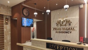 Un área de recepción con un mostrador de mármol, un reloj y un televisor montado en la pared.