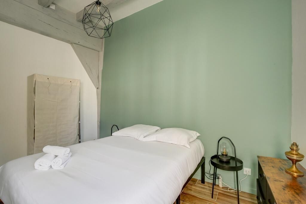 A neatly made bed with white linens and towels, a geometric light fixture above, and a small table with a lamp beside it.