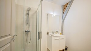 A modern bathroom with a glass shower enclosure, a white vanity with a mirror, and a wooden slat ceiling. - Amboise Une Vie de château (Tours)
