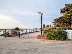 Un camino pavimentado con barandilla metálica, farol y pared de ladrillo con un letrero.
