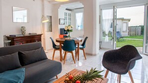 Ein modernes Wohnzimmer mit einer Couch, einem Couchtisch mit Obst, einem Essbereich mit Stühlen und einer roten Pendelleuchte.