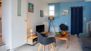 Ein modernes Wohnzimmer mit Fernseher, Stehlampe, Esstisch mit Obst, Sofa und blauer Wand.
