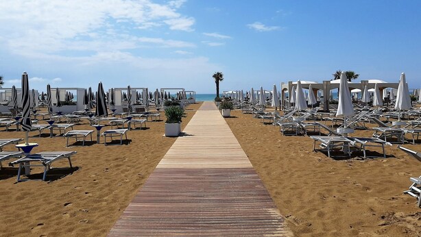A beach with rows of sun loungers and umbrellas, a wooden walkway, and a clear sky. - Belvilla by OYO Appartamento Rosso (Jesolo)