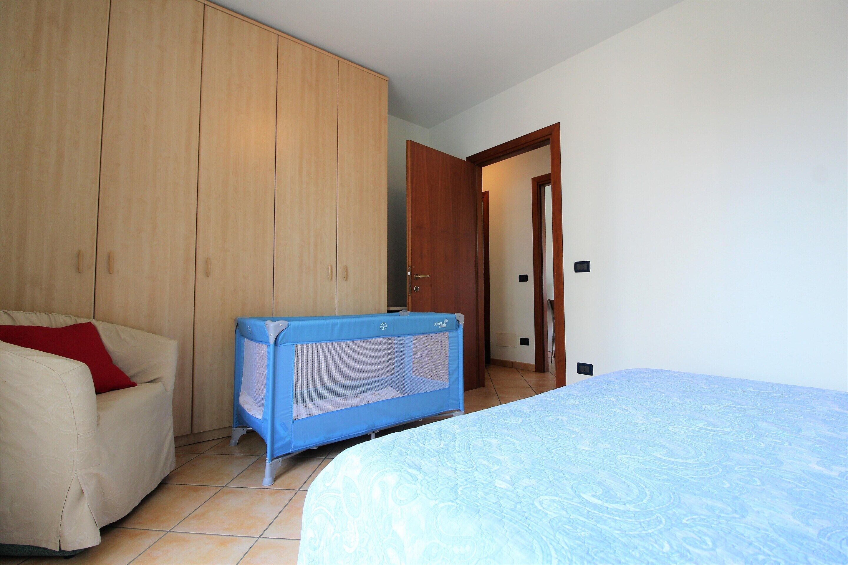 Un dormitorio con cama, sofá, armario de madera y corralito para bebé.