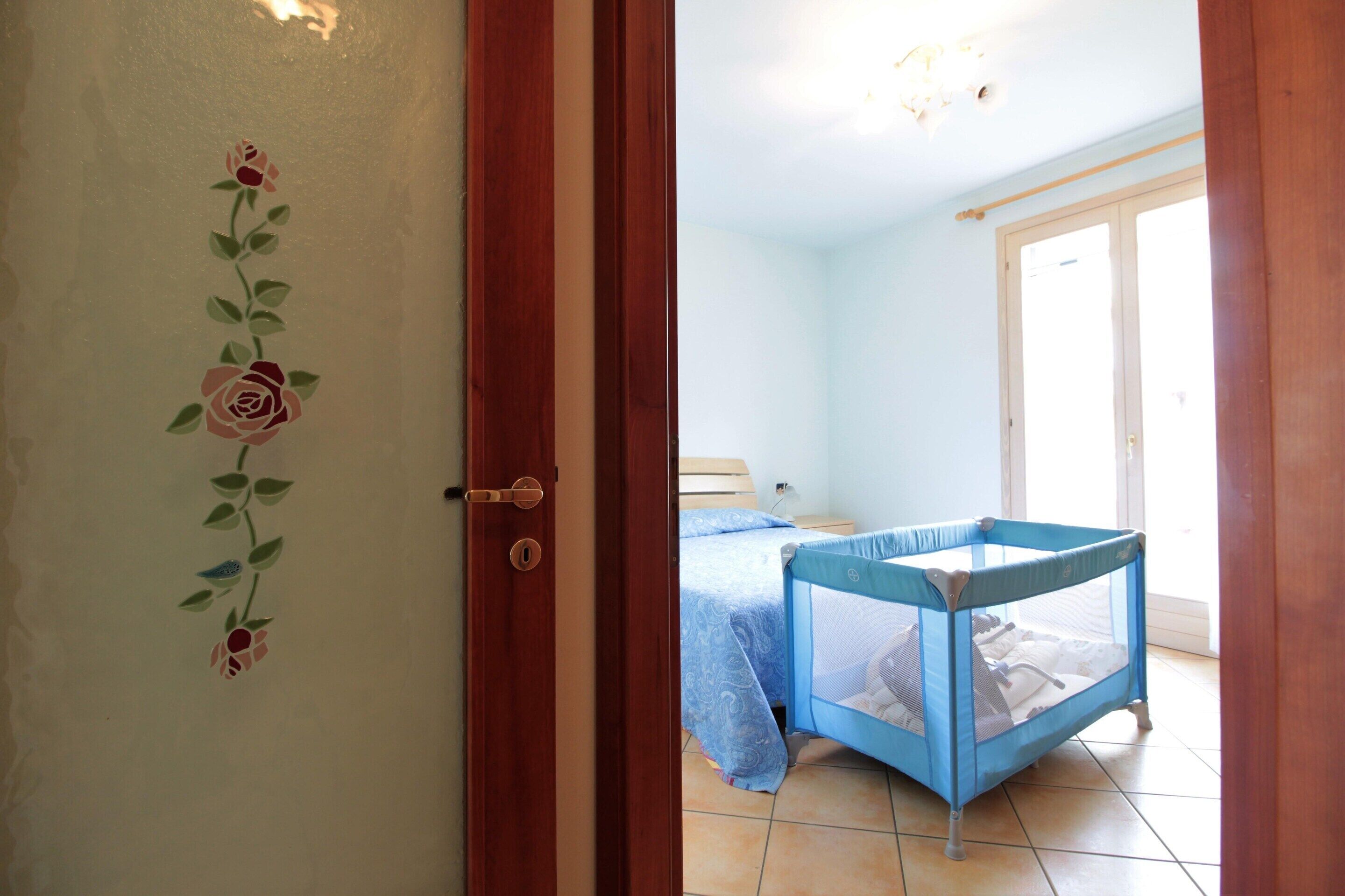 A room with a bed, a blue crib, and a door with a floral design.