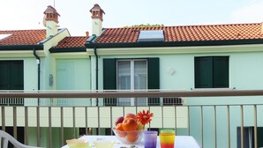 A balcony with a table set for a meal, featuring a bowl of fruit, a vase with flowers, and two colorful glasses. - Belvilla by OYO Appartamento Rosso (Jesolo)