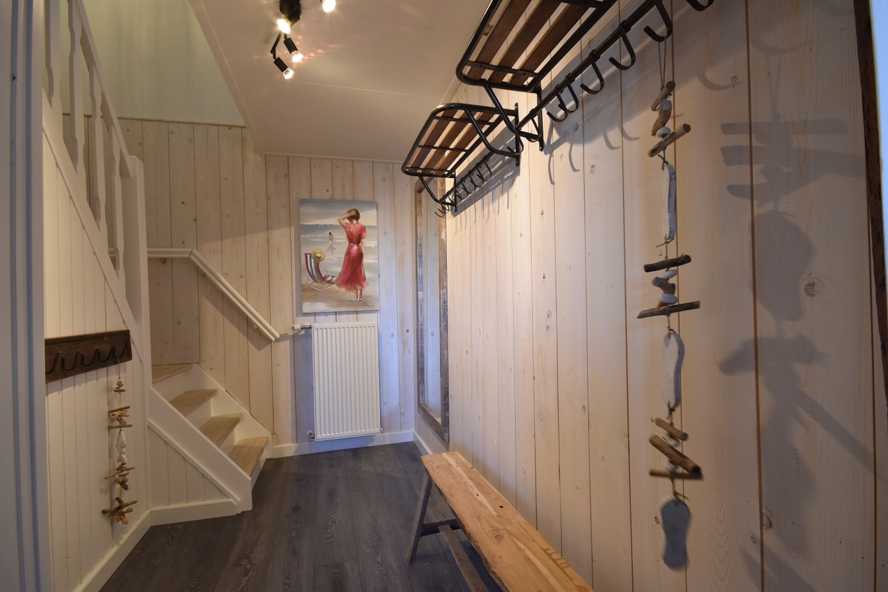 A wooden interior hallway with a staircase, a bench, and a wall-mounted rack.