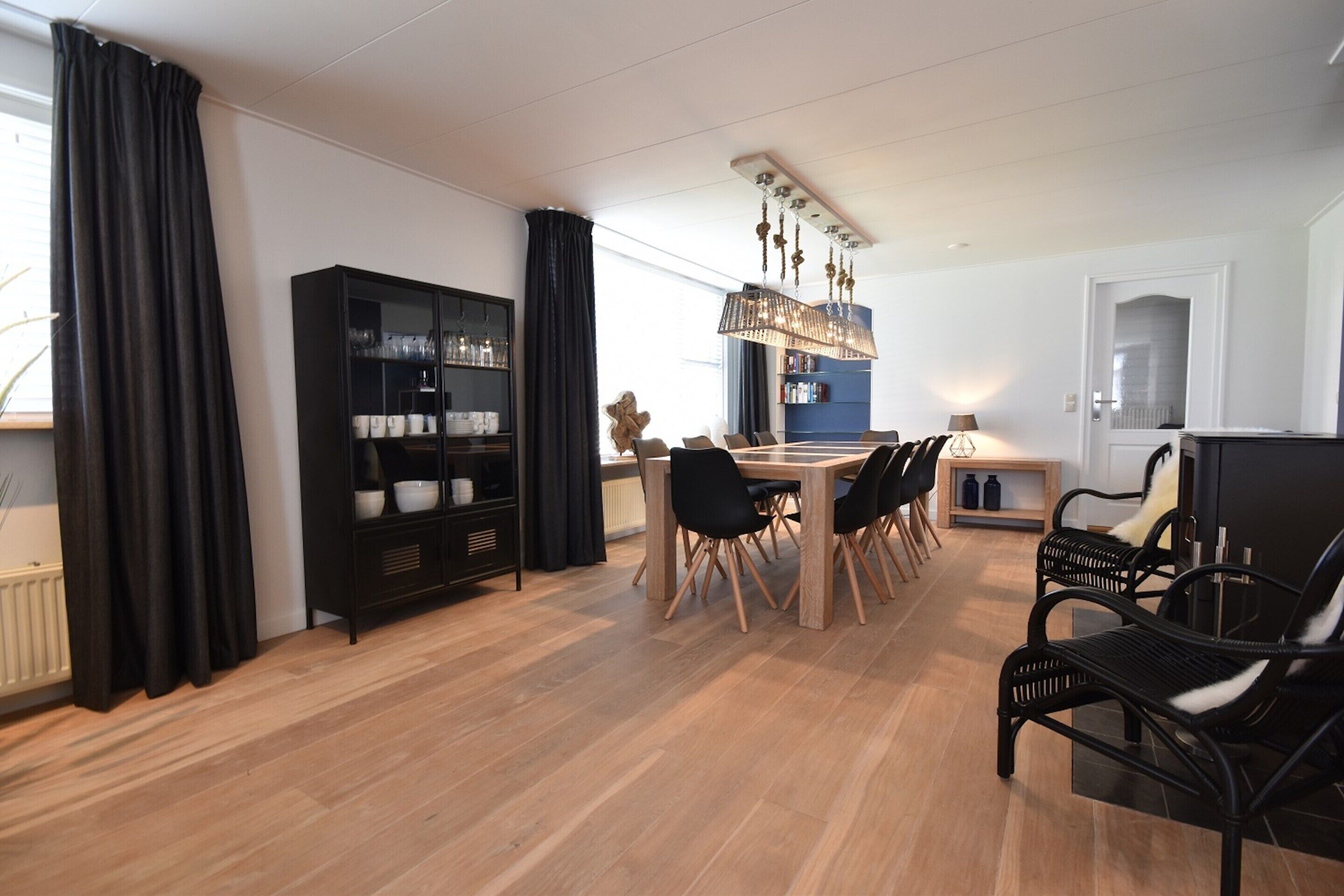 Una sala de estar moderna con comedor, que incluye un mueble negro, una mesa de comedor de madera con sillas y una lámpara de araña.