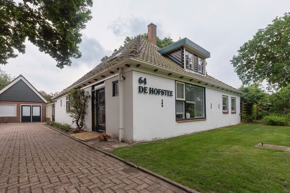 A single-story building with the number 64 DE HOFSTEE on its facade, a brick driveway, and a well-maintained lawn. - Farmhouse in North Holland Near Beaches (Sint Maartensvlotbrug)
