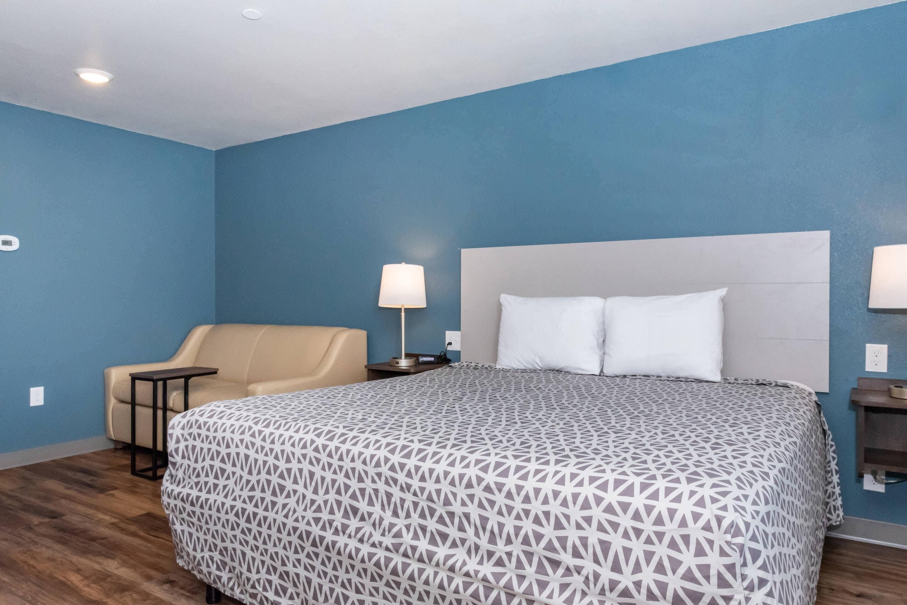 Une chambre d’hôtel avec un lit, une chaise, une table de chevet et une lampe.