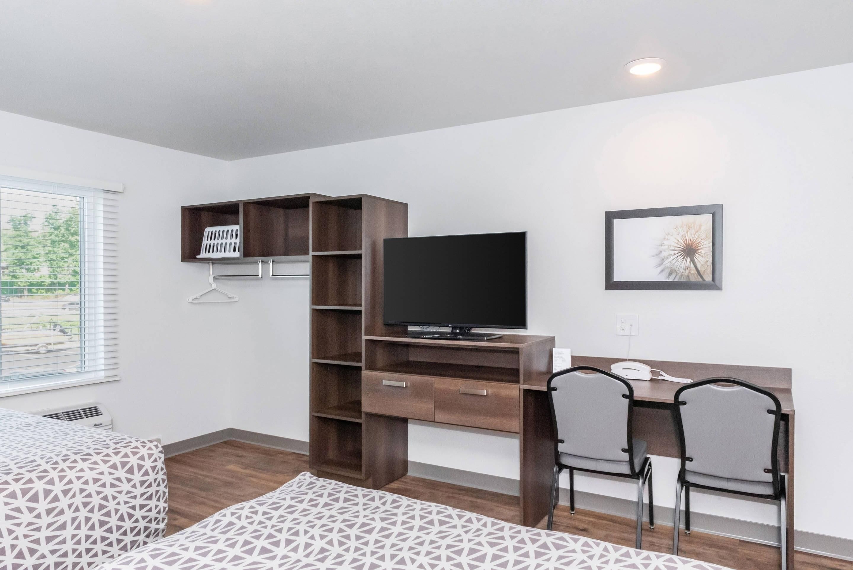 A hotel room with a bed, a desk with a TV, a chair, and a window with blinds.
