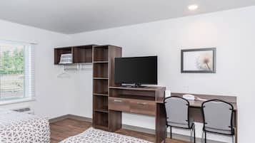 Habitación de hotel con cama, escritorio, televisión, una silla y ventana con persianas.