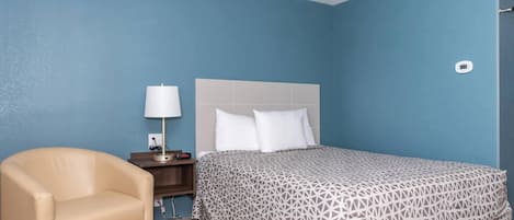 Habitació d'hotel amb llit, una cadira, una taula de nit, una làmpada i un termòstat.