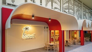 Een restaurant met een modern ontwerp, met een gebogen rode en witte gevel, terras en een neonreclame.
