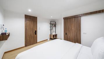 Una habitación de hotel moderna con una cama grande, un armario de madera y un pequeño estante con artículos de aseo.