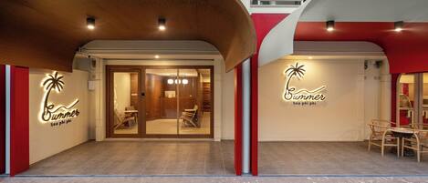 A modern building with a curved wooden overhang, glass doors leading to an interior with seating, and a sign reading "Summer Sea phi phi".