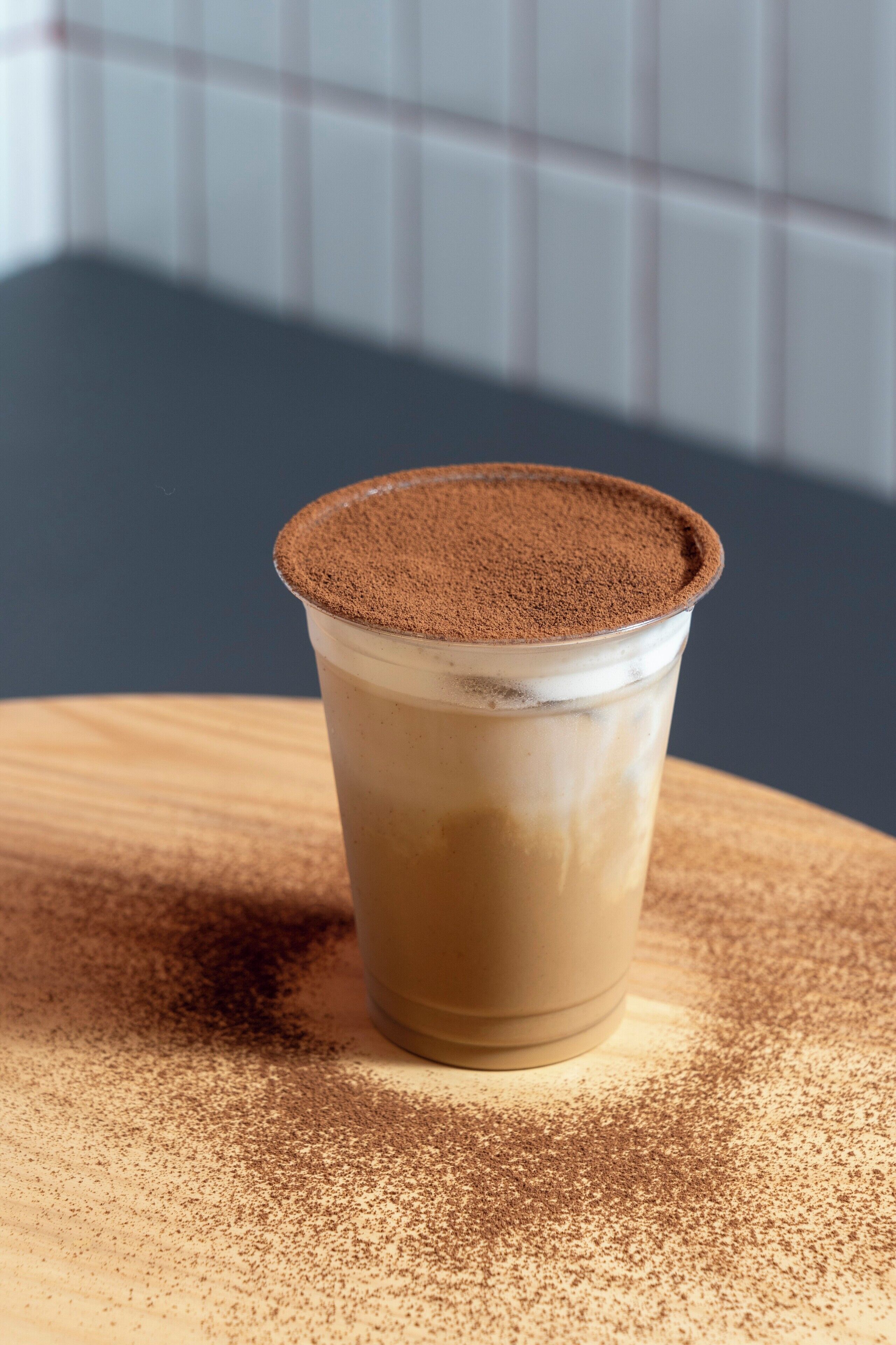 Een kop koffie met een laagje cacaopoeder erop, op een houten ondergrond.