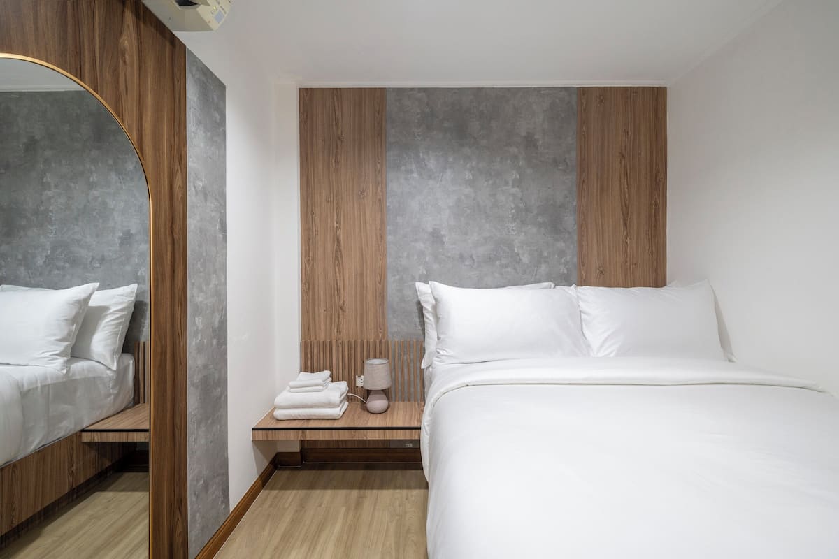 A modern hotel room with a large bed, a bedside table with a lamp, and a mirror.